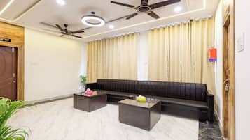 A modern living room with a black leather sofa, two glass coffee tables, a ceiling fan, recessed lighting, and a large window with curtains.
