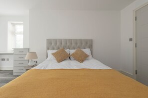 Un dormitorio con cama, dos almohadas, una mesita de noche con lámpara y un armario.