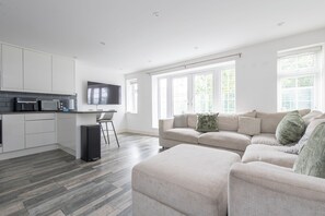 Een moderne woonruimte met een keuken, een zithoek en een aan de muur bevestigde televisie.