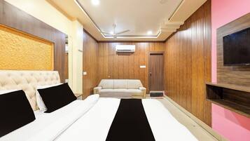 A hotel room with a bed, a sofa, an air conditioning unit, and a television.