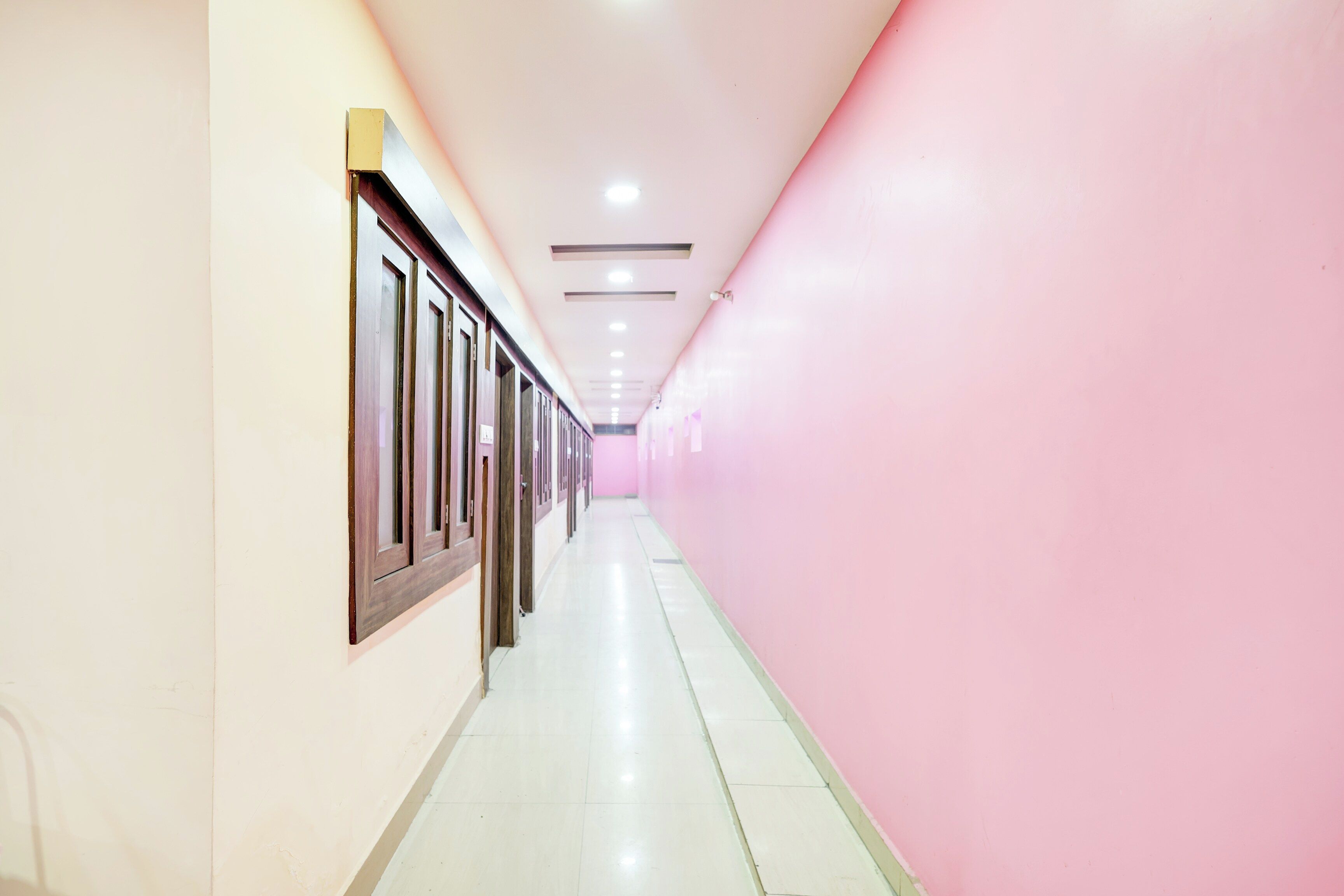 A corridor with doors on one side and a pink wall on the other.