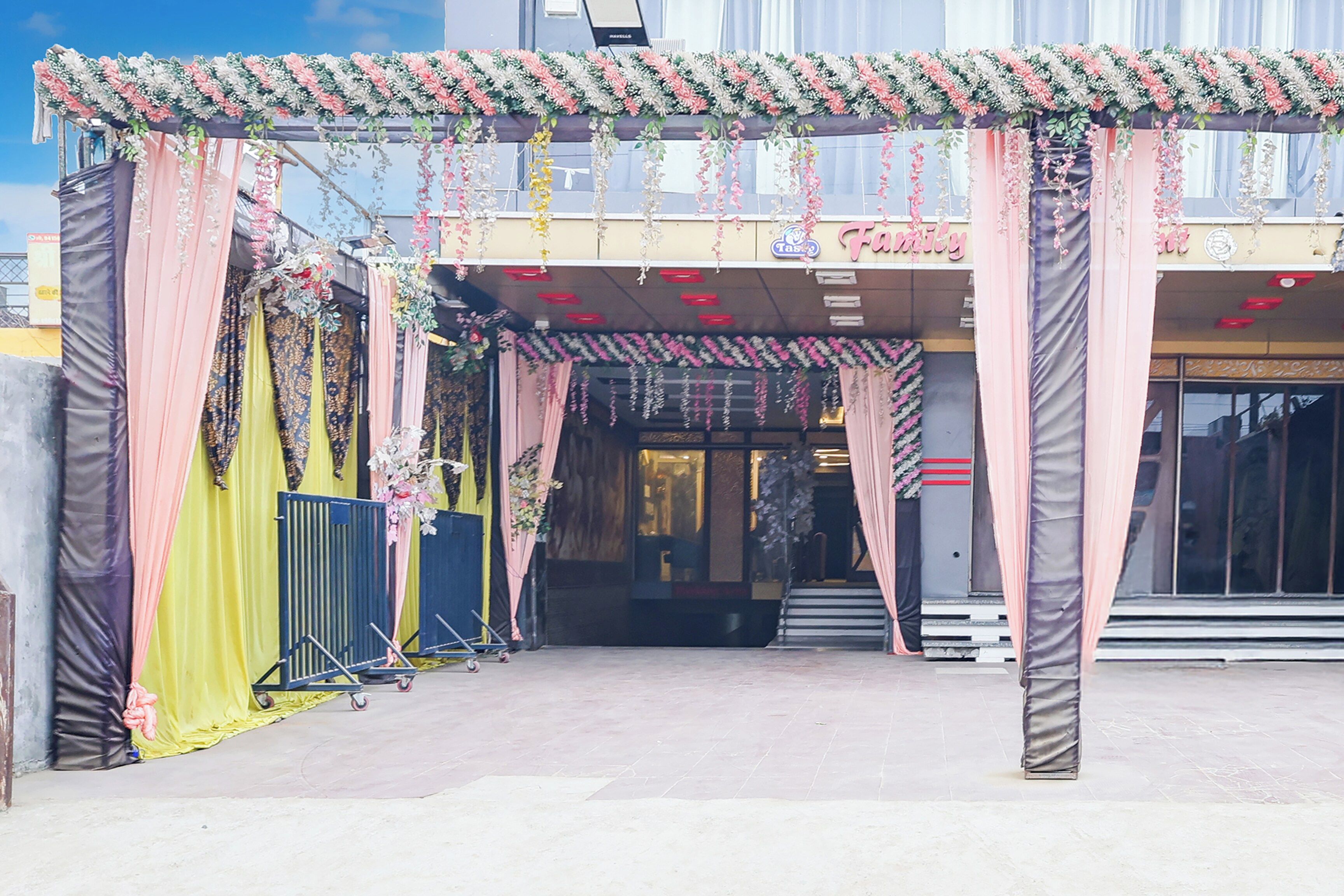 A building entrance with a covered walkway, decorative floral arrangements, and a sign above the entrance.