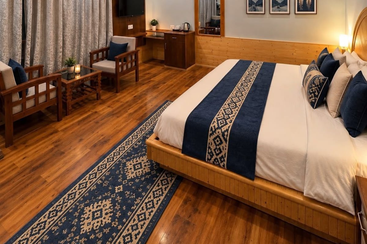 A hotel room with a wooden ceiling, a large bed with patterned bedding, a desk, and a seating area with chairs.