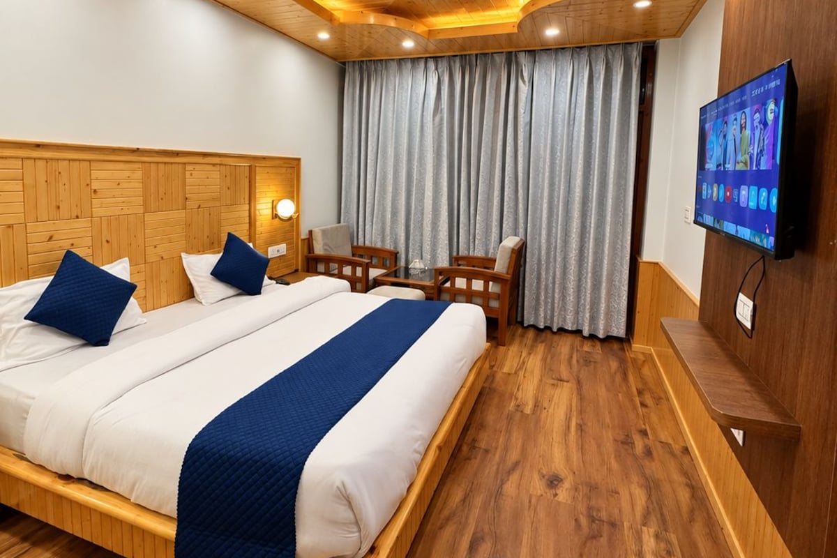 A hotel room with a wooden ceiling, a bed with blue bedding, a TV on the wall, and a wooden bench.