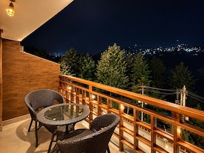 A balcony with wicker furniture and a glass table, overlooking a cityscape at night. - Hotel Old Manali Retreat (Manali)