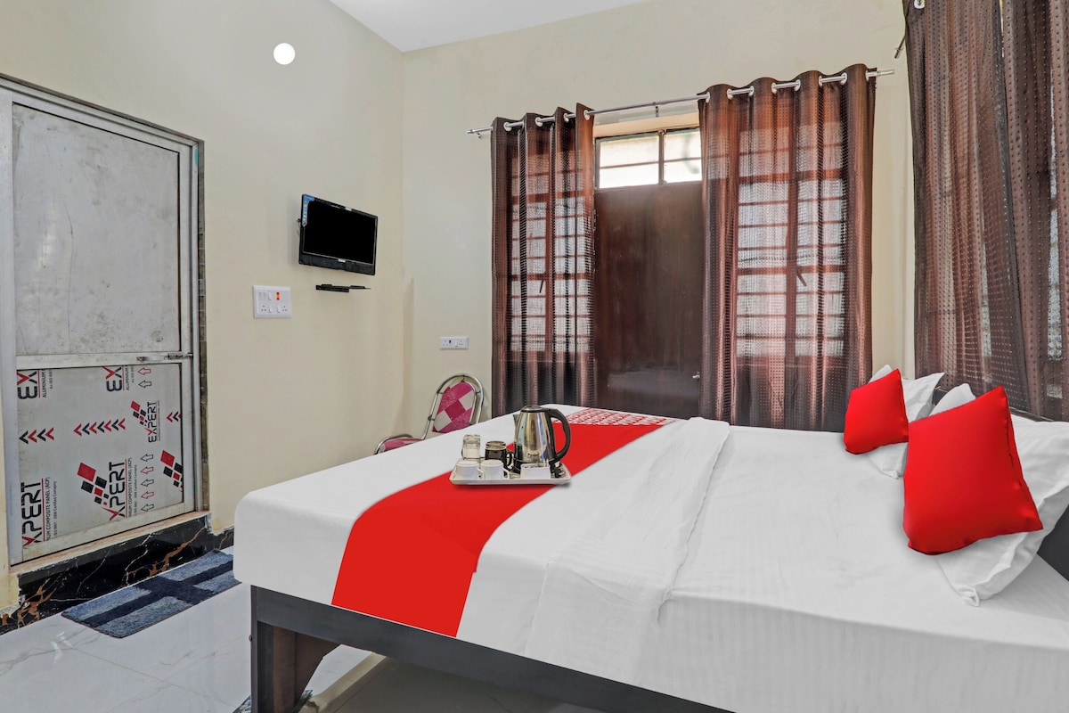 A hotel room with a bed, a TV, a window with curtains, and a door.