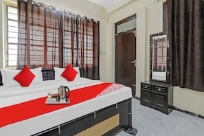 A hotel room with a bed, a bedside table, a mirror, and a window with curtains. - Hotel O Sunrise Inn (Gorakhpur)
