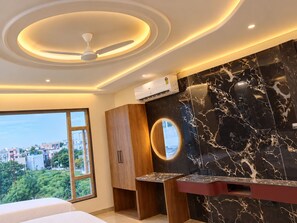 A modern bathroom with a ceiling fan, a vanity with a marble countertop, and a large window offering a city view. - Hotel Benchmark Suites (indore)