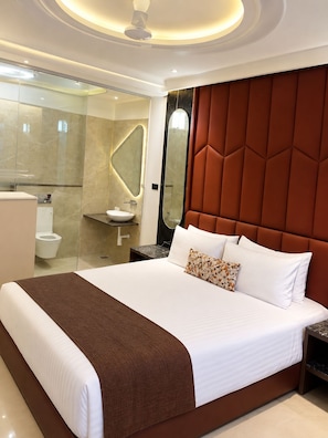 A modern hotel room with a large bed, a bathroom with a glass shower enclosure, and a marble-topped vanity. - Hotel Benchmark Suites (indore)