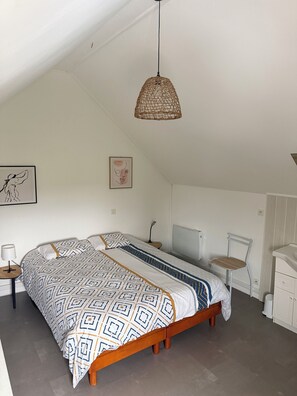 A bedroom with a bed, a chair, a desk, and a hanging light fixture.