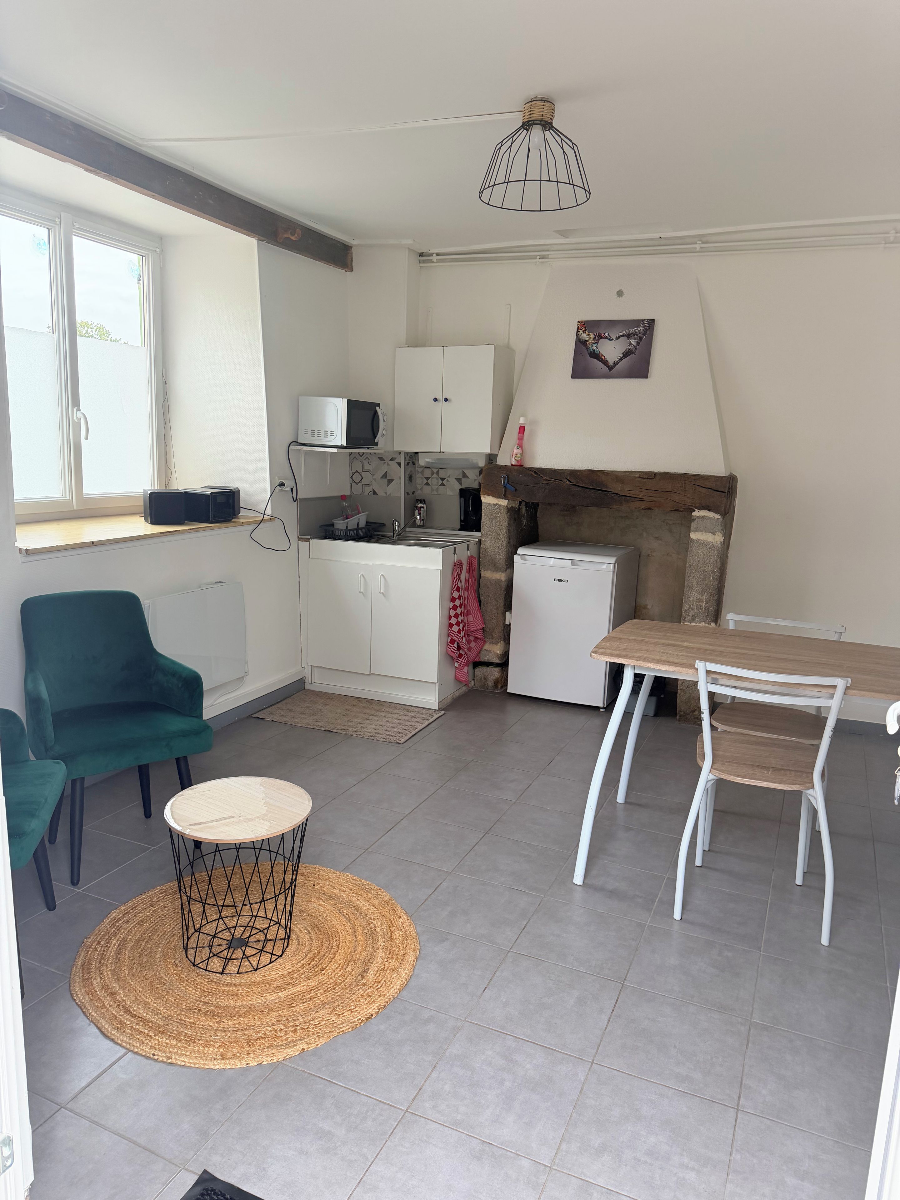 En kompakt opholdsstue med et tekøkken, spiseplads med bord og stole, sofa og en dekorativ lampe.