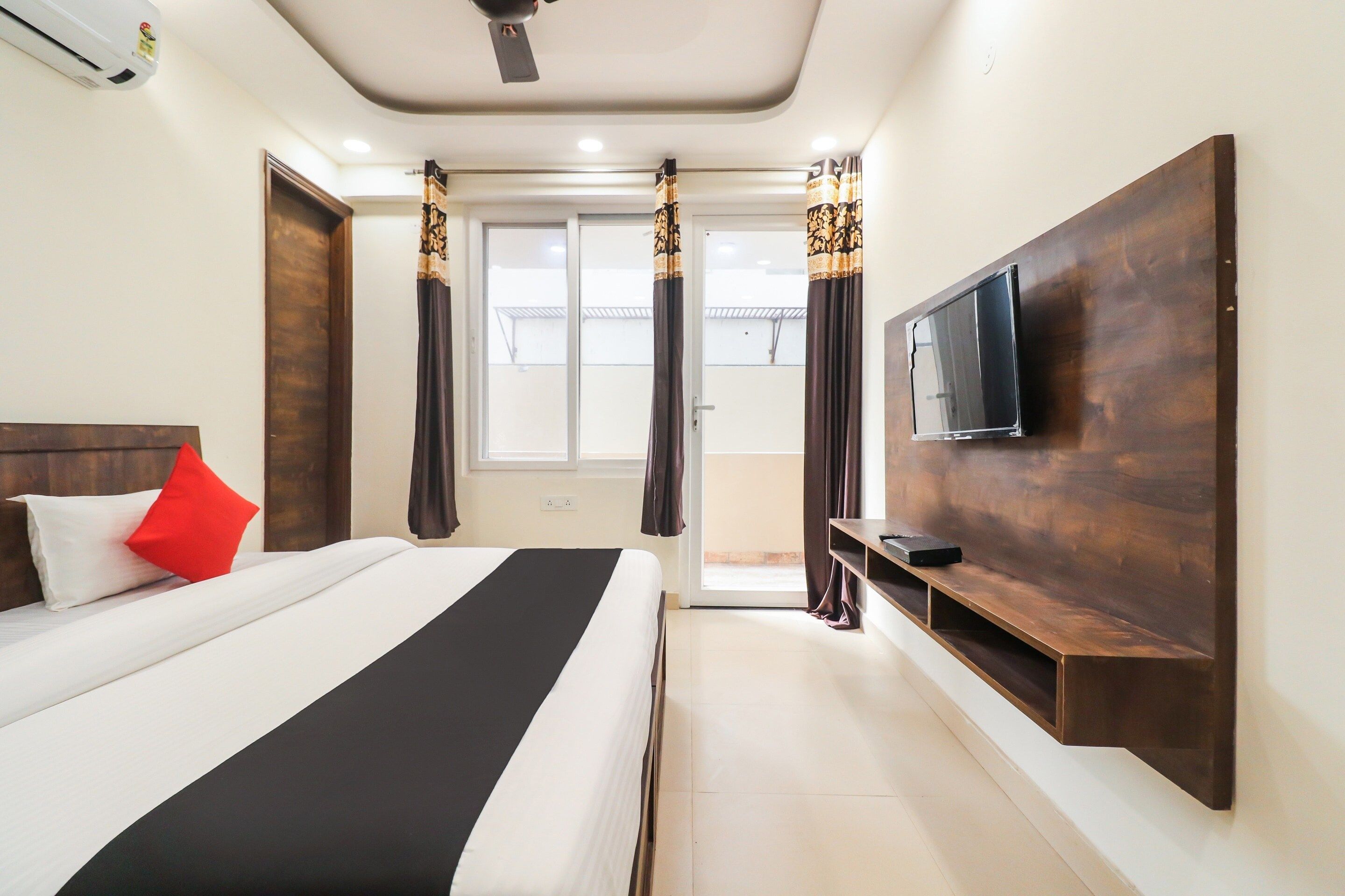 A hotel room with a bed, a TV mounted on the wall, and a window with curtains.
