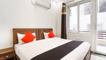 A hotel room with a bed, a wooden headboard, a window with curtains, and an air conditioning unit on the wall.