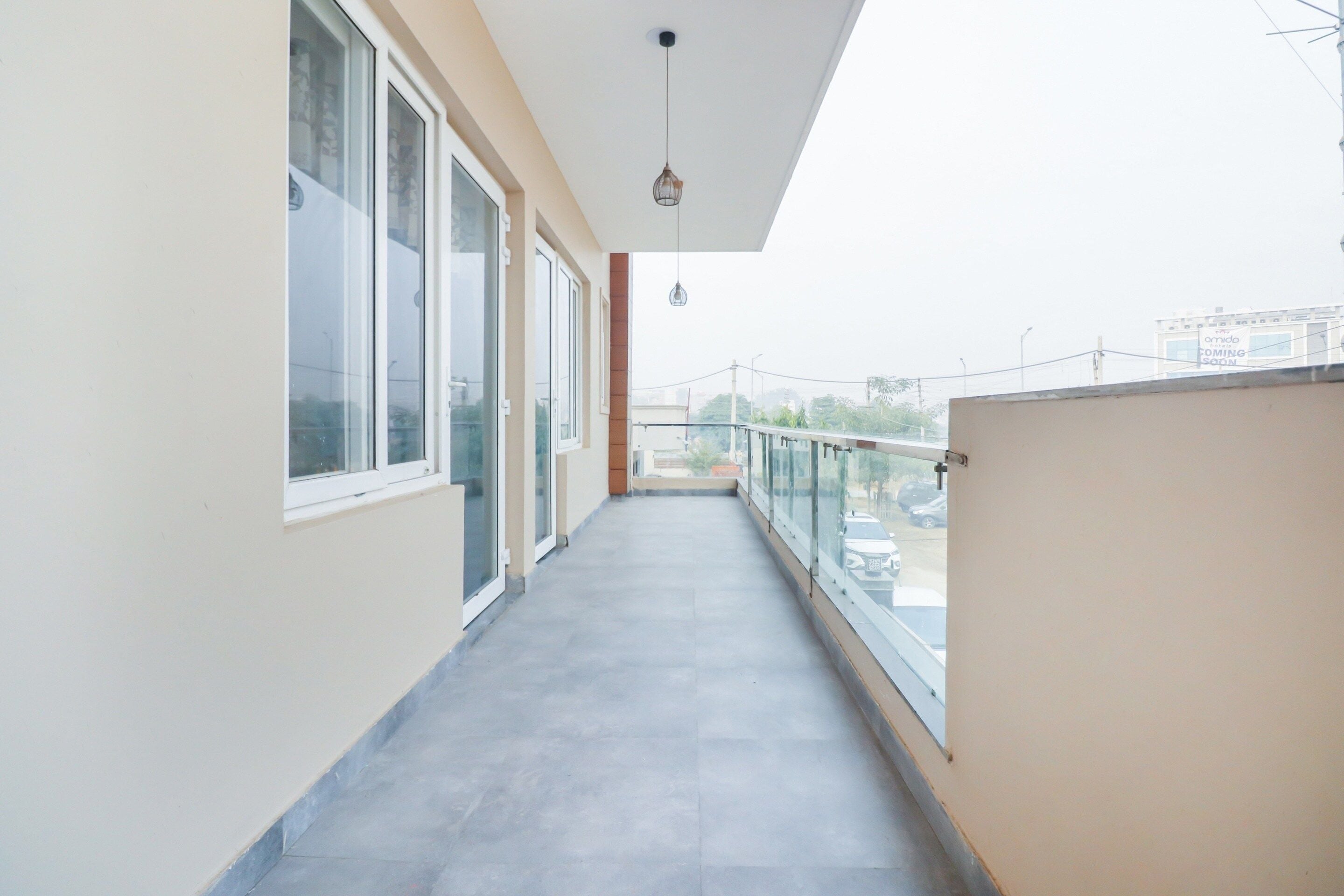 Ein Flur mit großen Fenstern auf einer Seite und einem Balkon mit Glasgeländer auf der anderen.