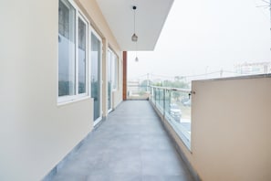A corridor with large windows on one side and a balcony with a glass railing on the other. - Collection O by OYO Green Leaf Residency (Gurgaon)