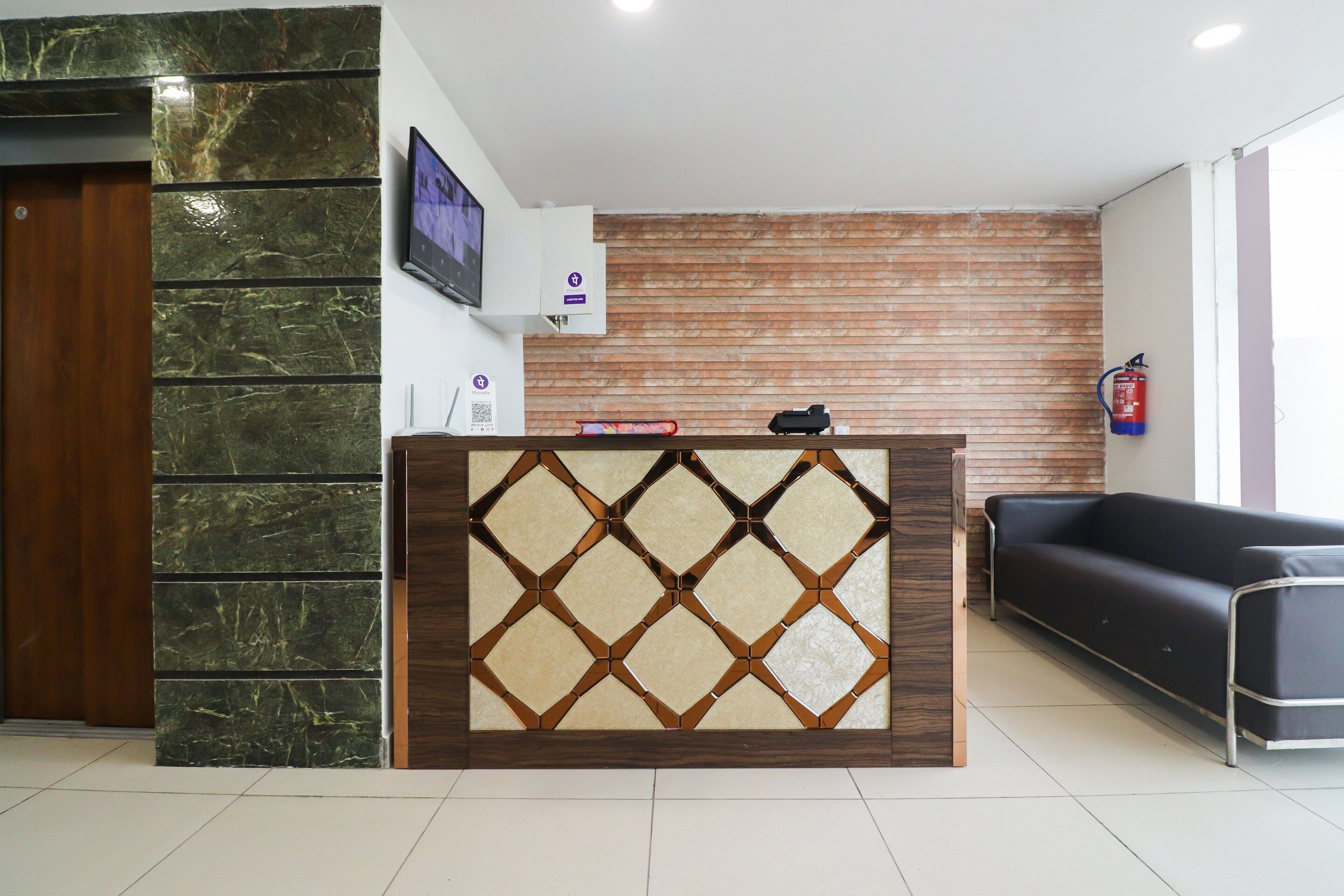 A reception desk with a marble and wood design, a mounted television, a fire extinguisher, and a black leather sofa.