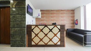 A reception desk with a marble and wood design, a mounted television, a fire extinguisher, and a black leather sofa.