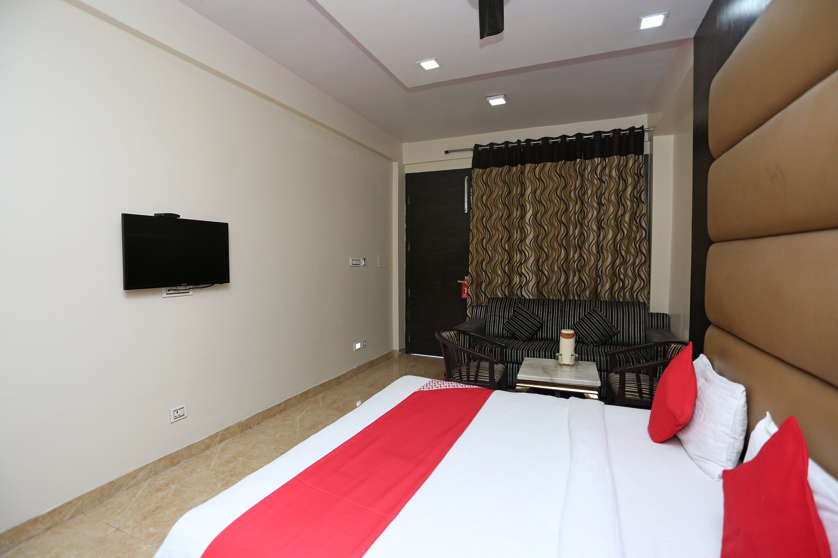 A hotel room with a bed, a television mounted on the wall, a sofa, and a table with a vase.