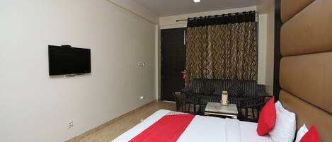 A hotel room with a bed, a television mounted on the wall, a sofa, and a table with a vase.