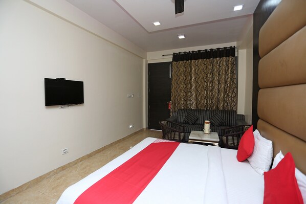 Habitación de hotel con cama, televisor montado en la pared, sofá y una mesa con un jarrón.