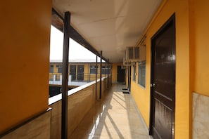 Un pasillo con piso de baldosas, barandilla de metal y una puerta con placa numérica.