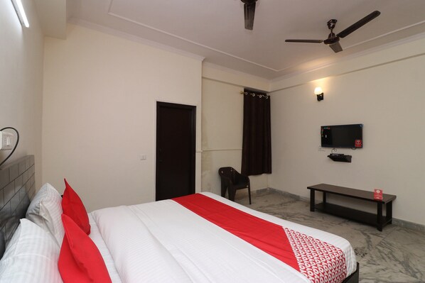 Una habitación de hotel con una cama, televisor, ventilador de techo, banco y una puerta.