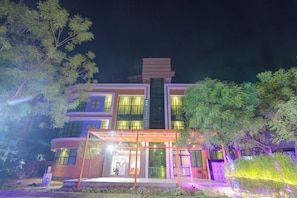 Un edificio de varios pisos con diseño moderno, que destaca por su entrada con puertas de vidrio y un área exterior cubierta.