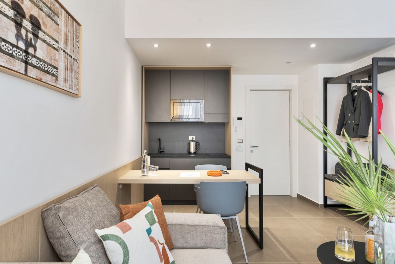 A modern living room with a sofa, a dining table, and a kitchen area with a microwave.
