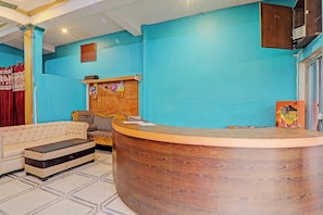 A reception area with a wooden reception desk, a sofa, a patterned armchair, and a cabinet. - Hotel O by OYO Siddharth Hotel And (Goshainganj)