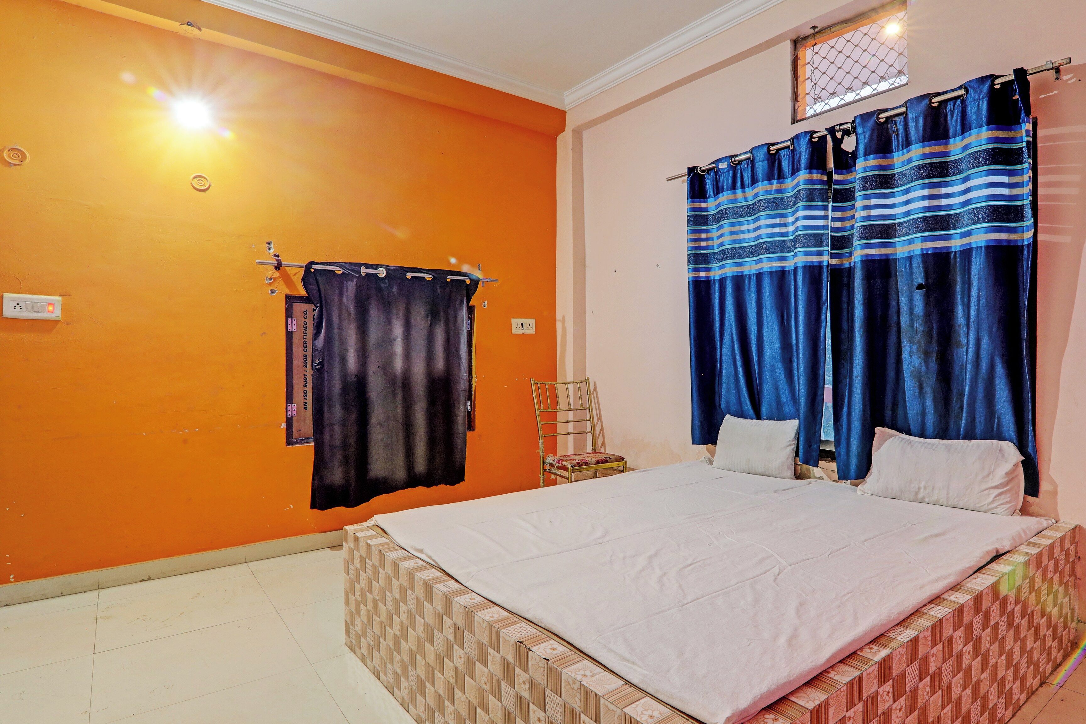 Ein Schlafzimmer mit einer orangefarbenen Wand, einem Bett mit weißer Bettwäsche und blauen Vorhängen.