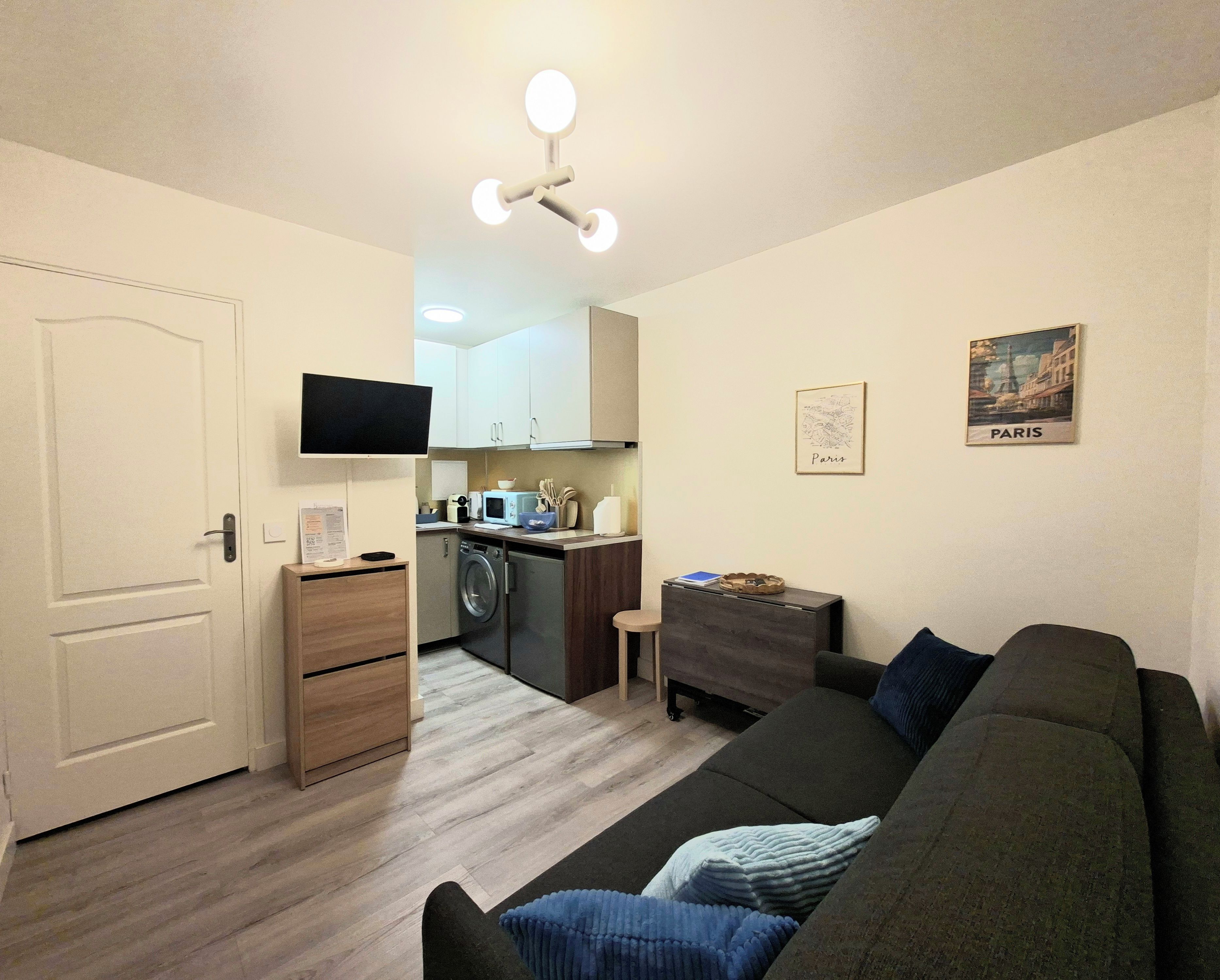 A compact living space with a kitchenette, a flat-screen TV, a sofa, and a small table.