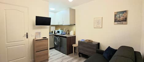 Un espacio habitable compacto con kitchenette, una televisión de pantalla plana, un sofá y una pequeña mesa.
