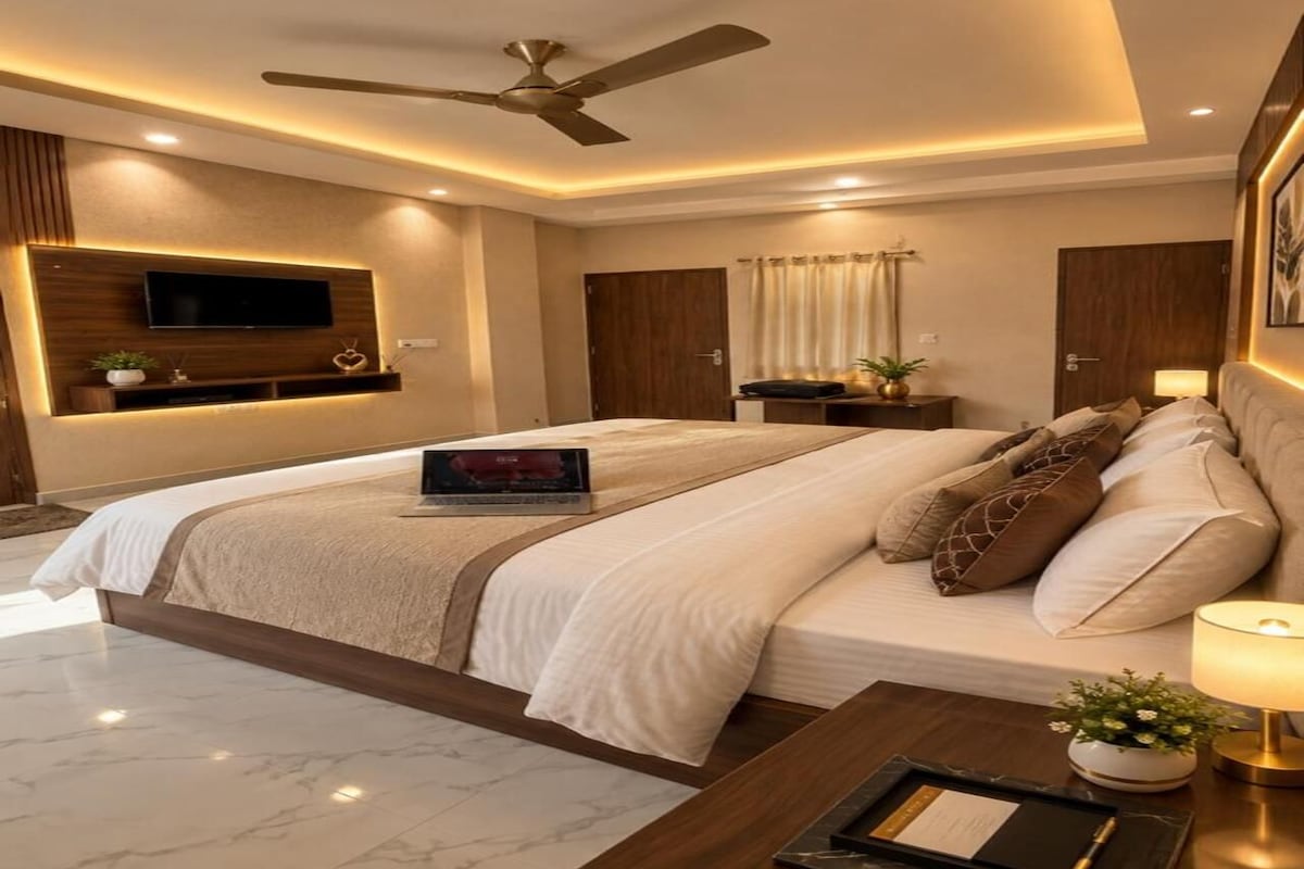 Een moderne slaapkamer met een groot bed, een flatscreen televisie aan de wand, een plafondventilator en een nachtkastje met een lamp.