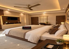 A modern bedroom with a large bed, a flat-screen TV mounted on the wall, a ceiling fan, and a bedside table with a lamp. - Kamla Palace Hotel (Amer)