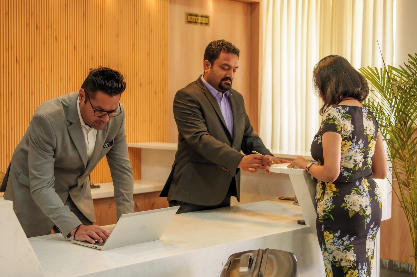 Una recepción con una computadora portátil, un hombre trajeado y una mujer con vestido estampado.