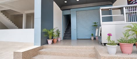 A modern building entrance with a staircase leading to a blue door, potted plants, and a signboard.