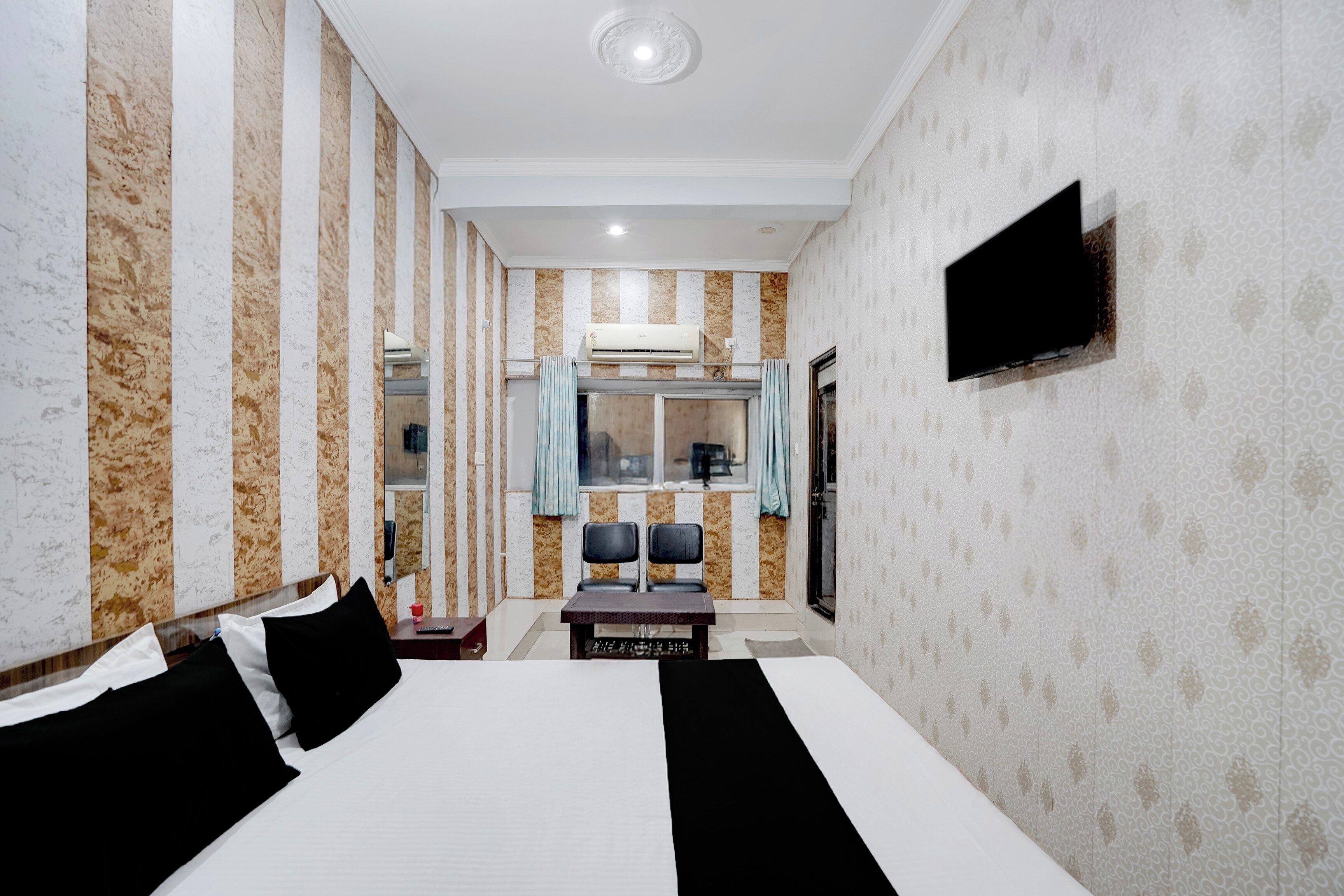 A hotel room with a large bed, a flat-screen TV mounted on the wall, a small table with chairs, and a window with curtains.