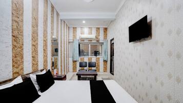 A hotel room with a large bed, a flat-screen TV mounted on the wall, a small table with chairs, and a window with curtains.