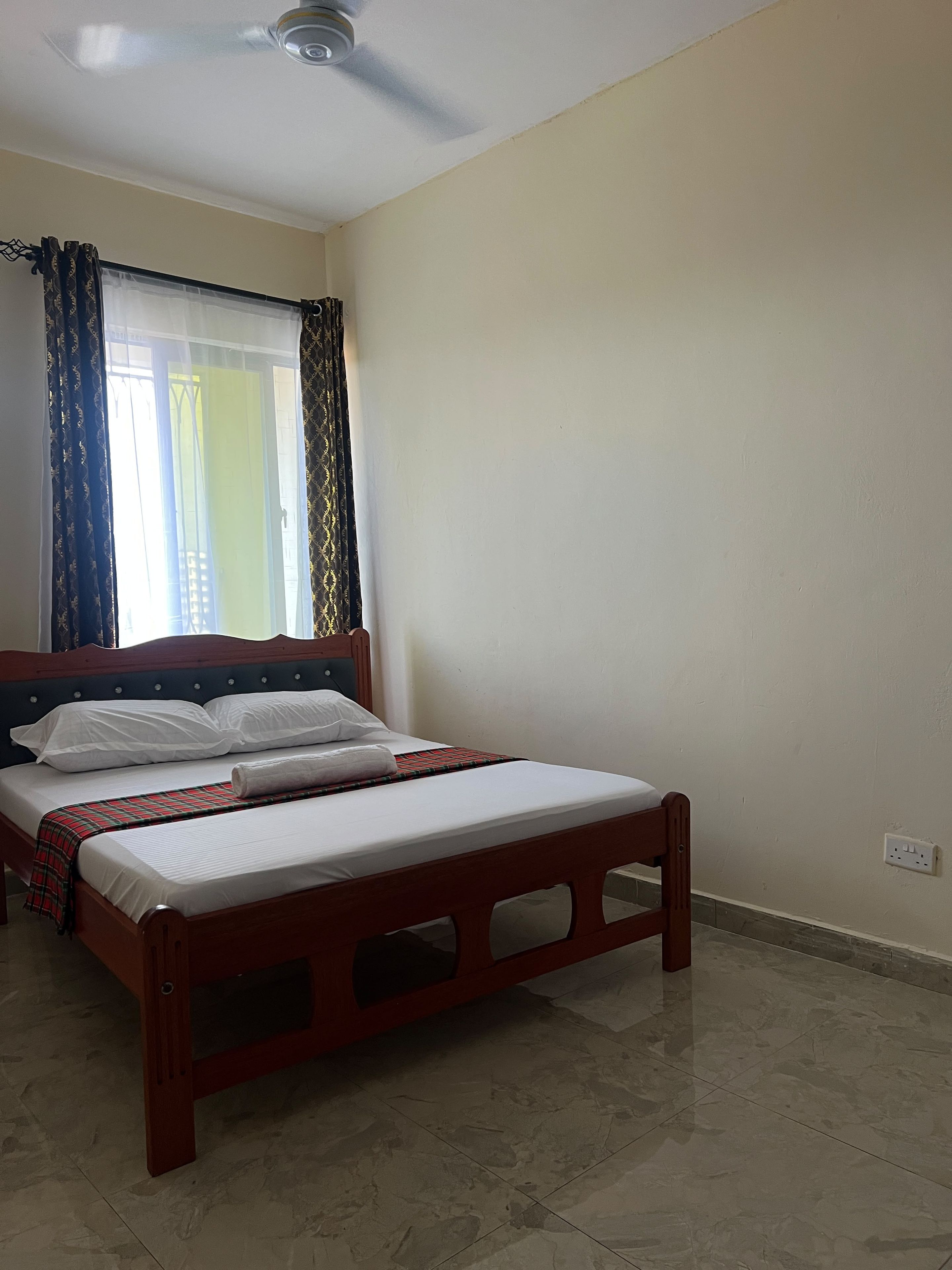 A bedroom with a bed, a ceiling fan, and a window with curtains.