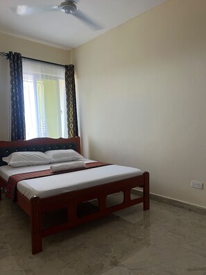 Une chambre à coucher avec un lit, un ventilateur de plafond et une fenêtre avec des rideaux.