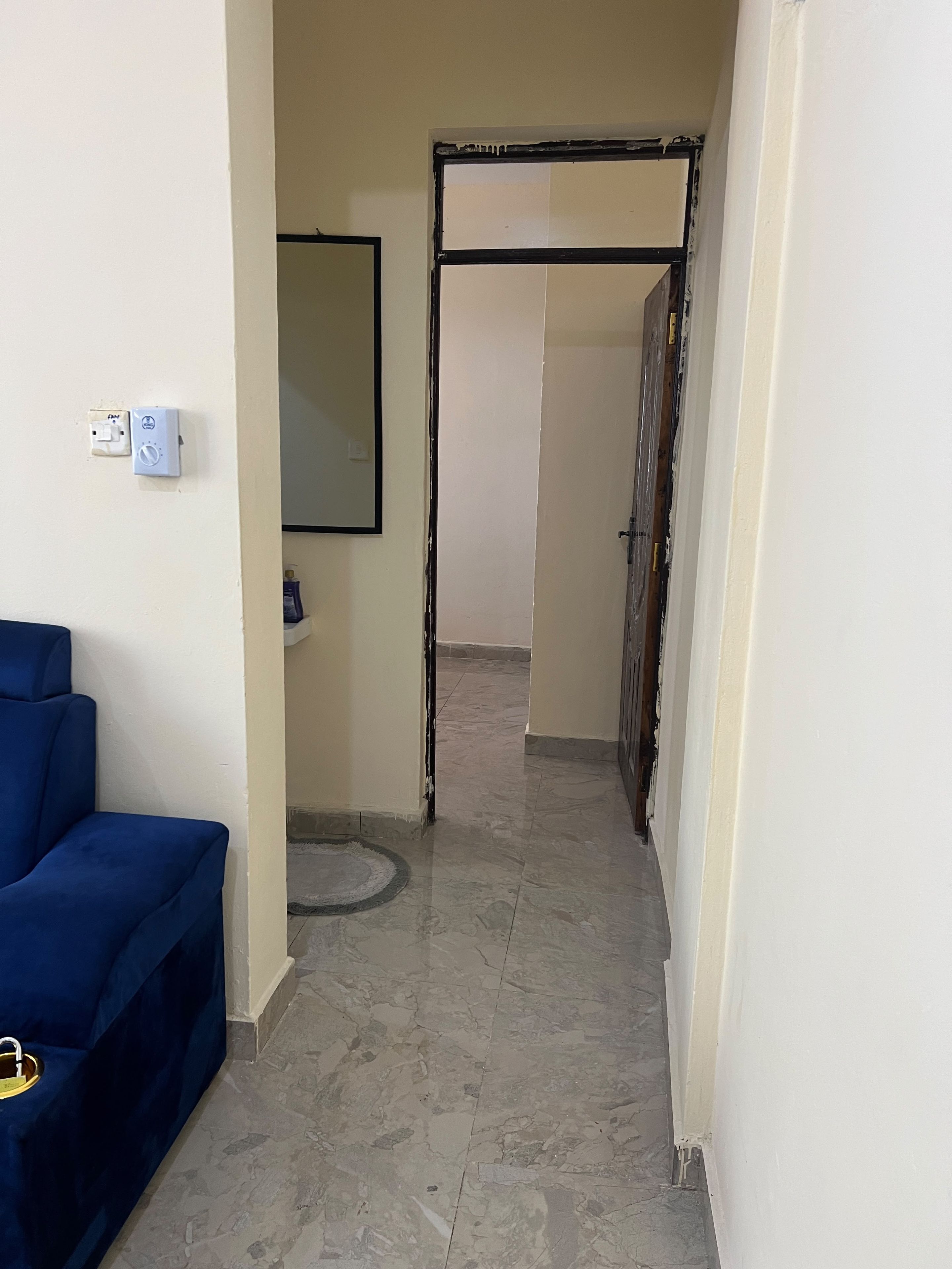 A hallway with a blue chair, a door frame, and a tiled floor.