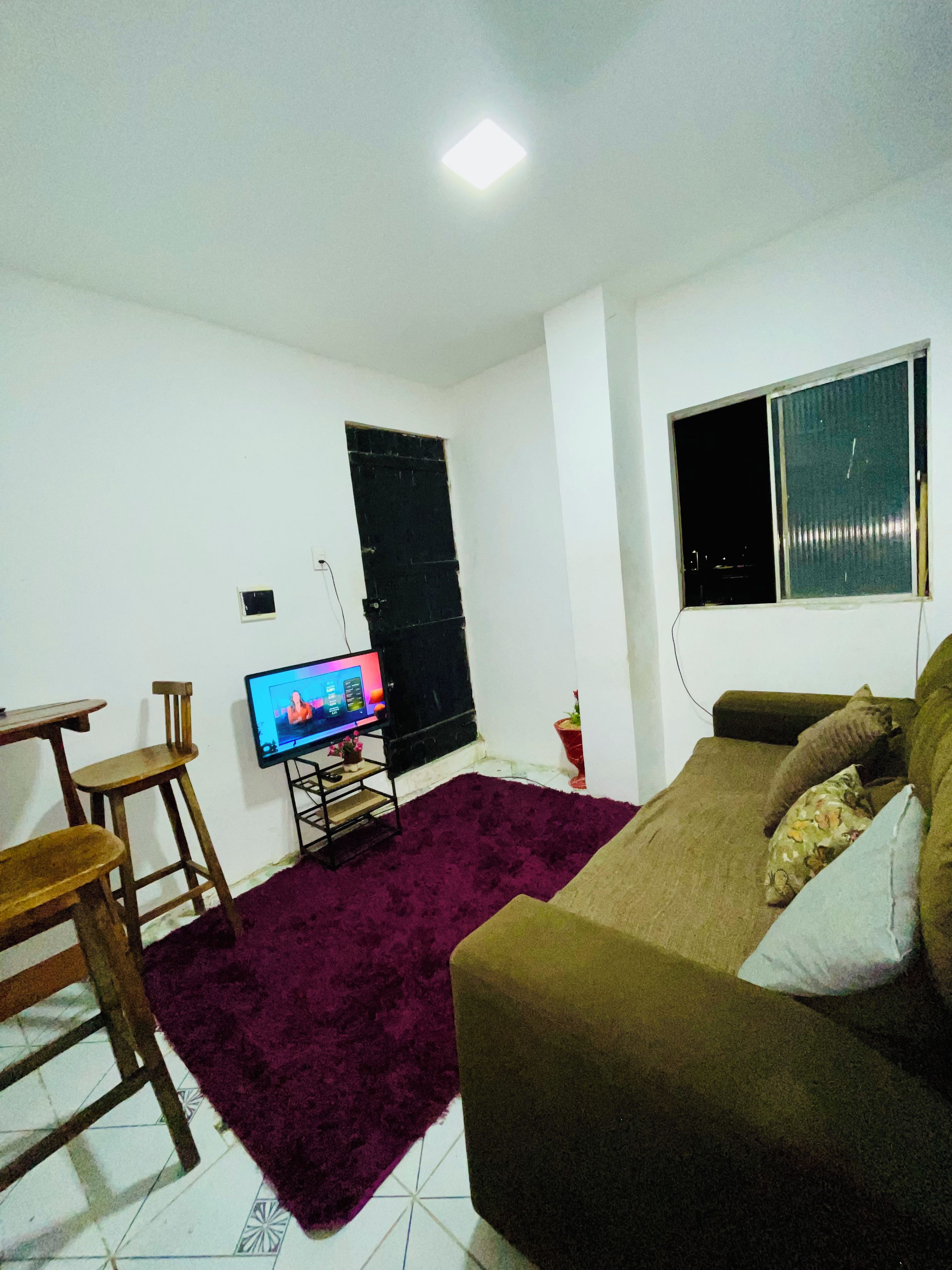 A living room with a television, a sofa, a small table, and a purple rug.
