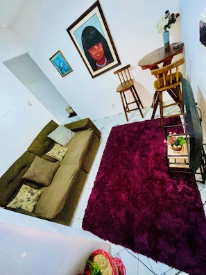 Een woonkamer met een bank, een rood tapijt, een eettafel met stoelen en een ingelijst schilderij aan de muur.