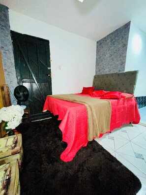 Een slaapkamer met een bed, een deur, een ventilator en een vloerkleed.