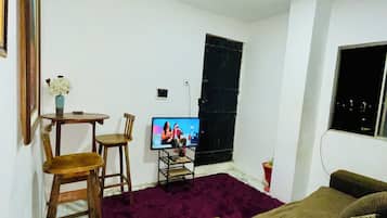 Habitació amb llit, televisió, taula petita amb cadires i finestra.