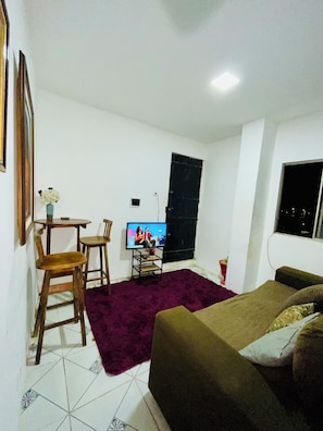 Una habitación con una cama, un televisor, una pequeña mesa con sillas y una ventana.