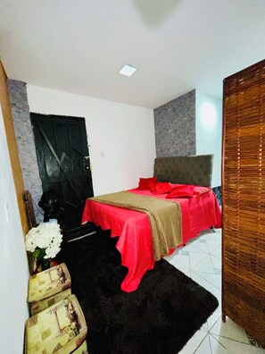 Een slaapkamer met een bed, een zwart tapijt, een houten garderobe en een witte deur.