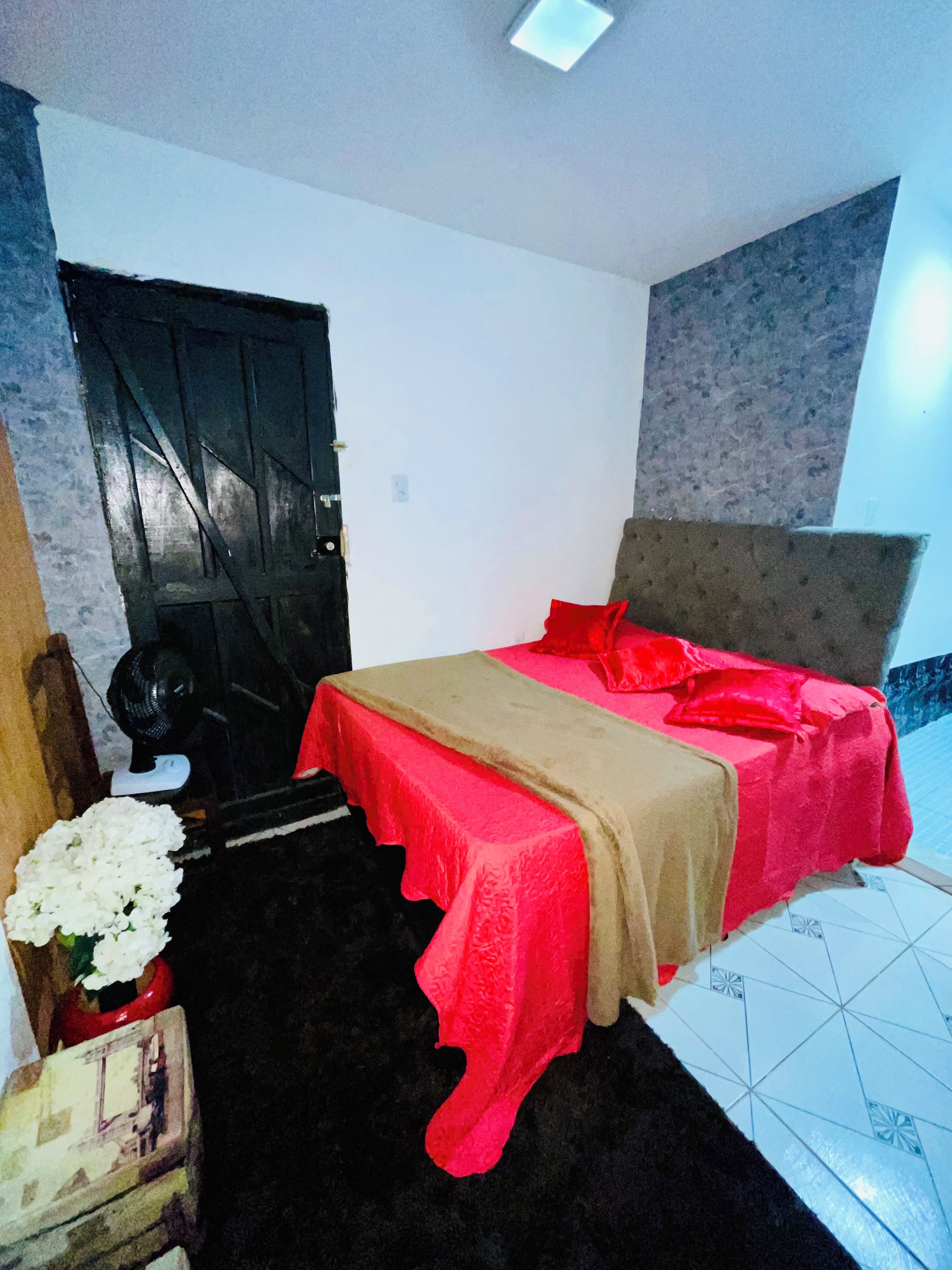 Een slaapkamer met een bed, een deur, een ventilator en een betegelde vloer.