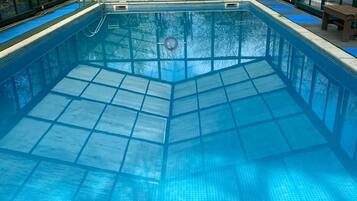 An indoor swimming pool with clear blue water, surrounded by a glass roof structure.