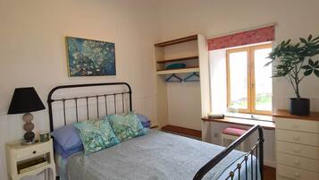 A bedroom with a bed, bedside table, lamp, window, and a painting on the wall.